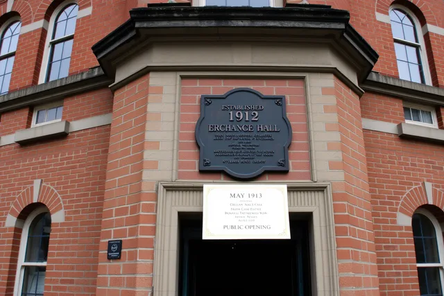 Historic brick exchange hall with bronze 1912 plaque and 1913 opening invitation. Fictional case: correcting a historic building's opening date