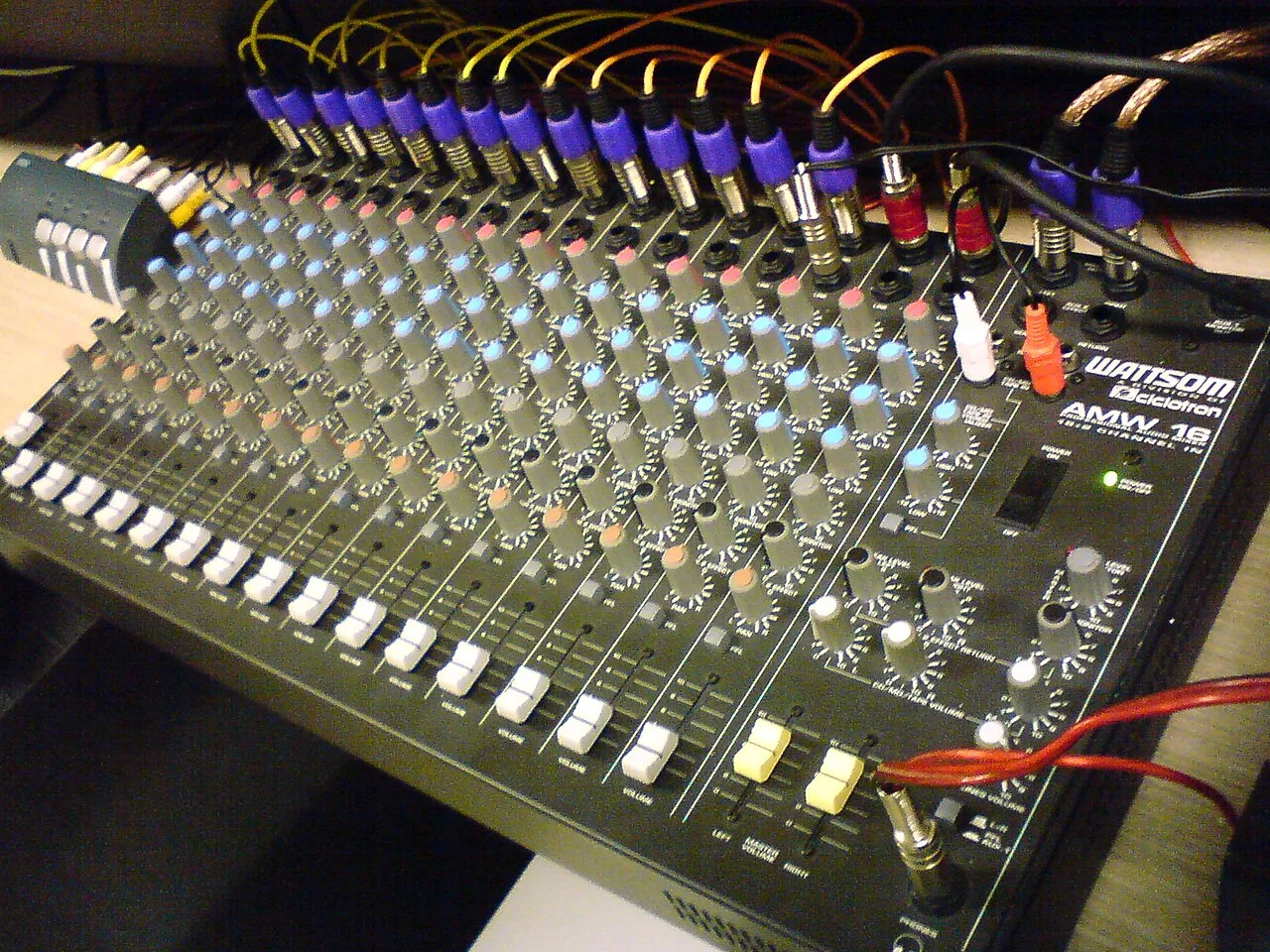 A sixteen-channel analog mixing console with connected cables, knobs, and faders