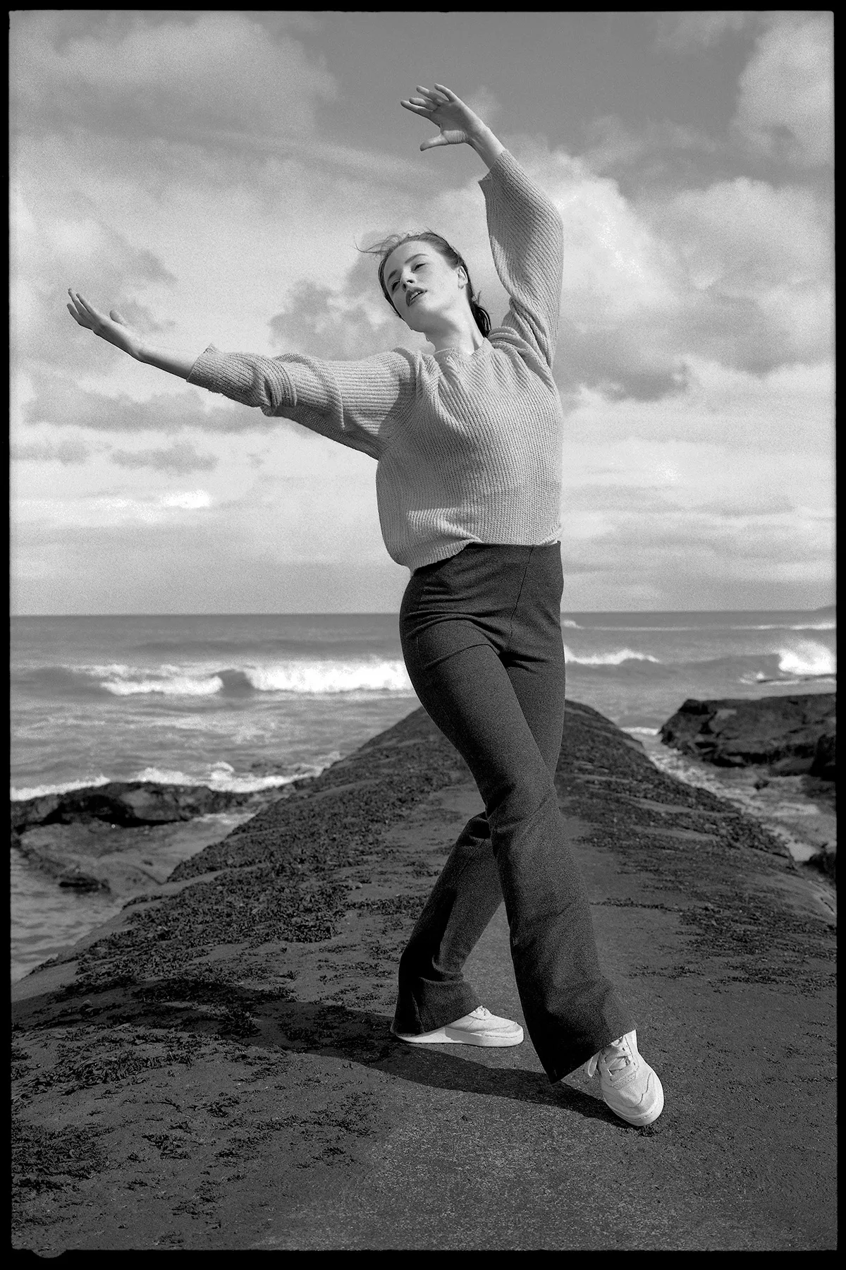 A black-and-white photograph of a contemporary ballet dancer moving outdoors near the sea